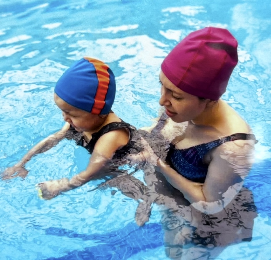 Mamá sonriendo con su bebé en brazos dentro de la piscina